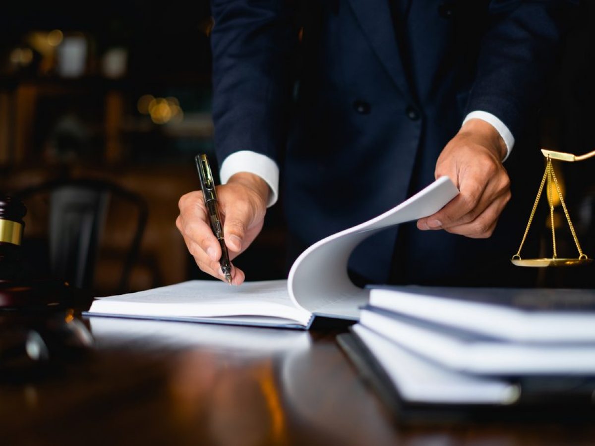 Lawyer writing notes with a pen on legal documents, gavel and scales of justice in the foreground, symbolizing the impact of DWI charges on legal professionals.